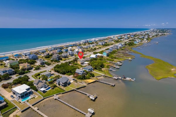 Aerial view of beachfront residential community with ocean, sandy beach, bay waterway, and docked boats